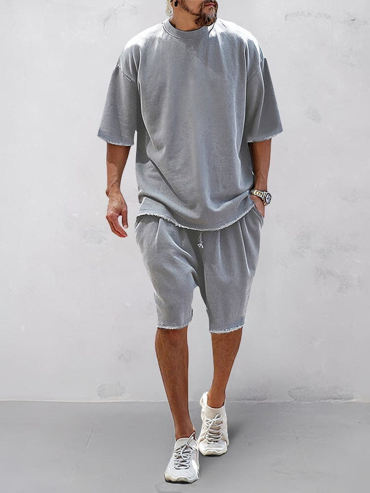 Front view of a model wearing a grey relaxed fit shorts and matching t-shirt with raw edge hems