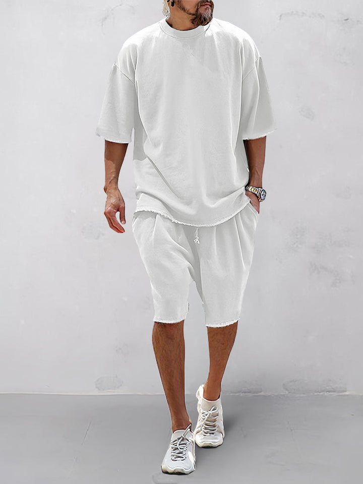 Front view of a model wearing a white relaxed fit shorts and matching t-shirt with raw edge hems