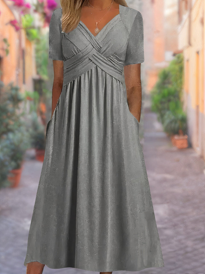 Front view of a grey V-neck dress with short sleeves, a ruched bodice, and pockets, worn by a model