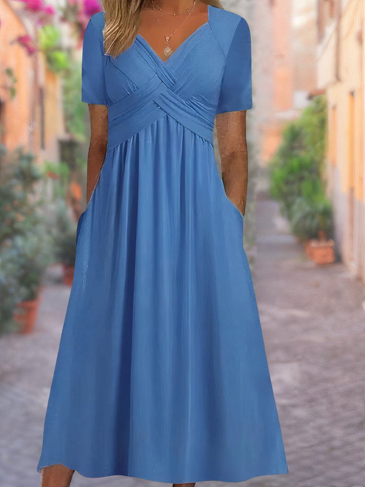 Front view of a blue V-neck dress with short sleeves, a ruched bodice, and pockets, worn by a model