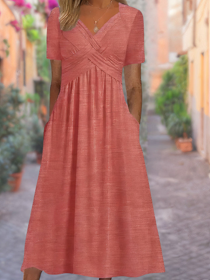 Front view of a peach V-neck dress with short sleeves, a ruched bodice, and pockets, worn by a model
