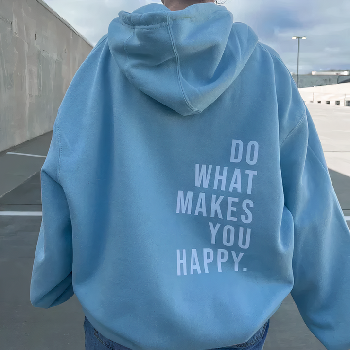 Back view, model in a blue relaxed knit pullover hoodie with "DO WHAT MAKES YOU HAPPY" text, outdoor setting