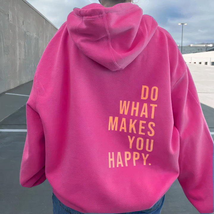 Back view, model in a pink relaxed knit pullover hoodie with "DO WHAT MAKES YOU HAPPY" text, outdoor car park