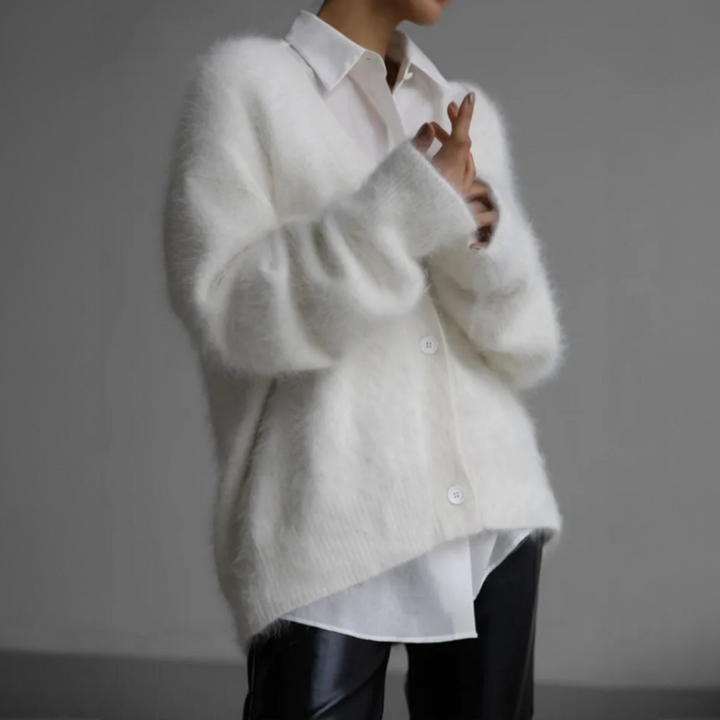 Front view of a model wearing a fluffy white oversized V-neck knit cardigan over a white shirt and black pants