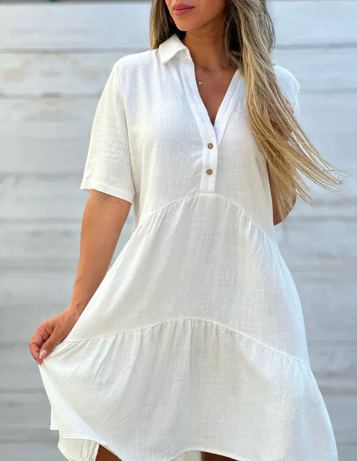 Close up of a model wearing a white loose blouse mini dress with a collared V-neck and tiered skirt