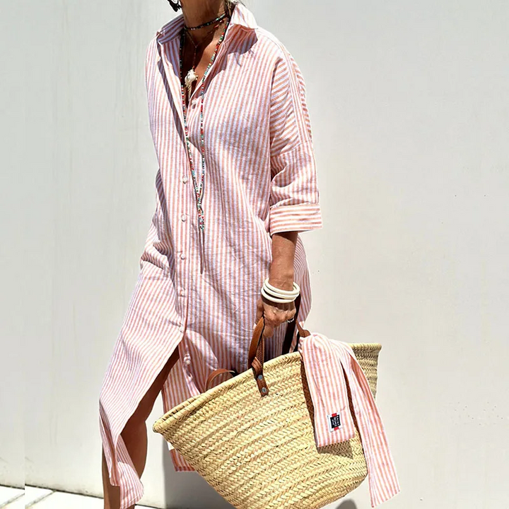 Front view of a model wearing a striped shirt dress, holding a straw bag with a matching striped fabric draped over it