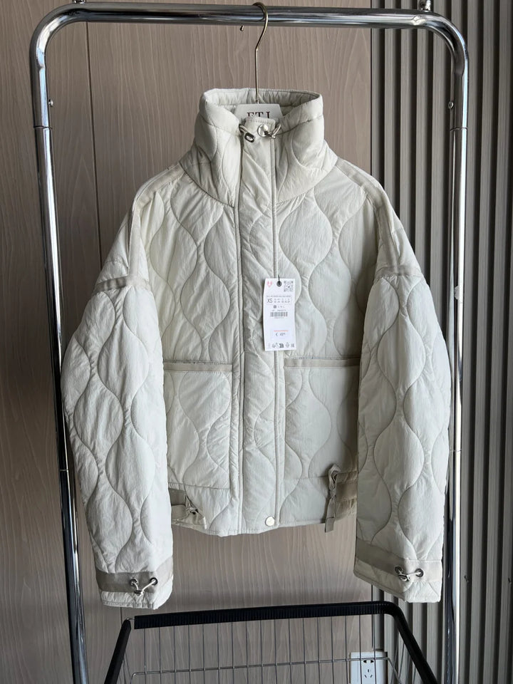 Front view of the cream quilted cotton Kara jacket with two front pockets and tie waist on a hanger