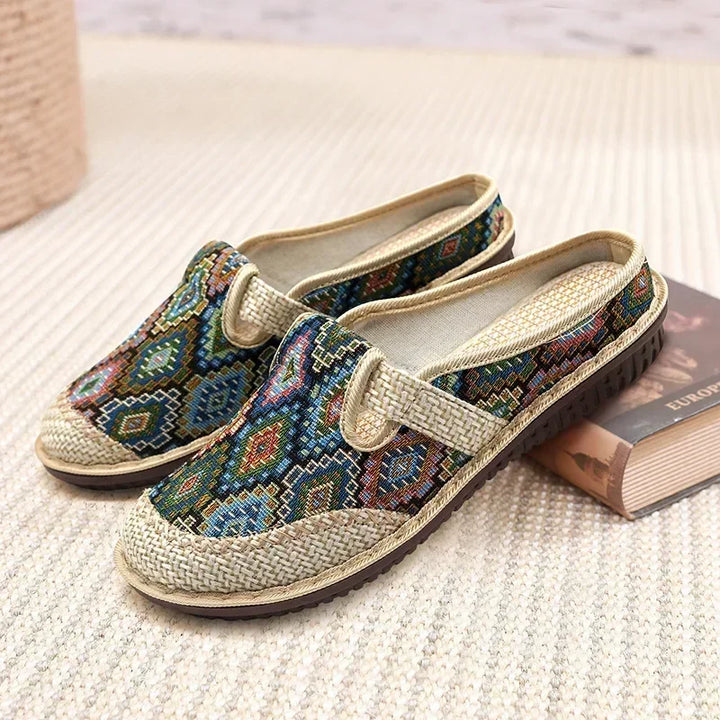 Three quarter view of two ethnic linen slip-on shoes with colourful embroidered patterns and woven straw details