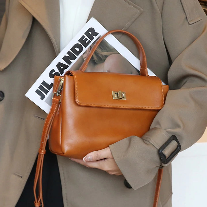 Close up of a brown Giselle leather tote bag held by a model, showing the top handle and gold turn lock