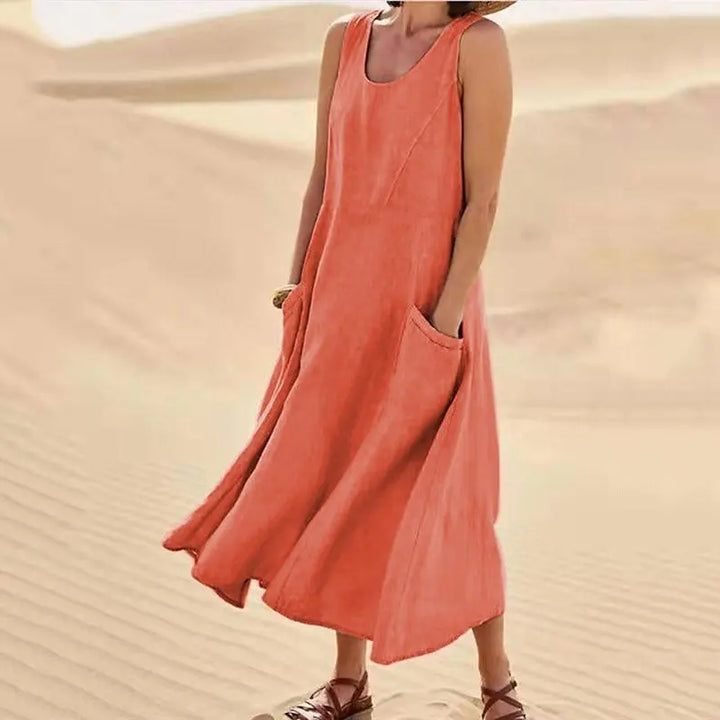 Three quarter view of Anna A-Line Sleeveless Midi Dress in coral with pockets, worn by model on sand dunes
