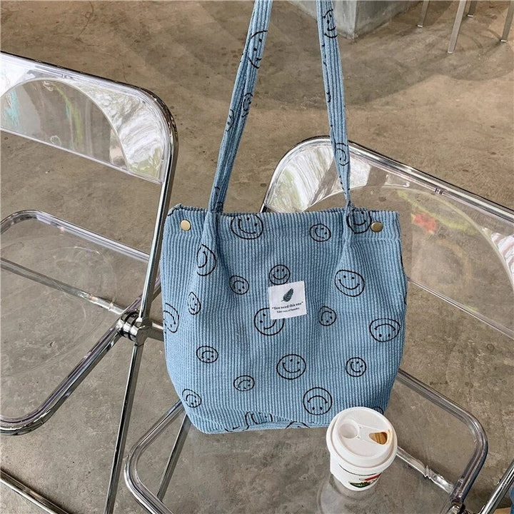Light blue smiley print corduroy tote bag on a clear chair