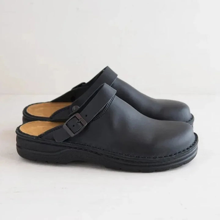 Side view of a pair of black PU leather slip-on shoes with black soles and light brown inner lining