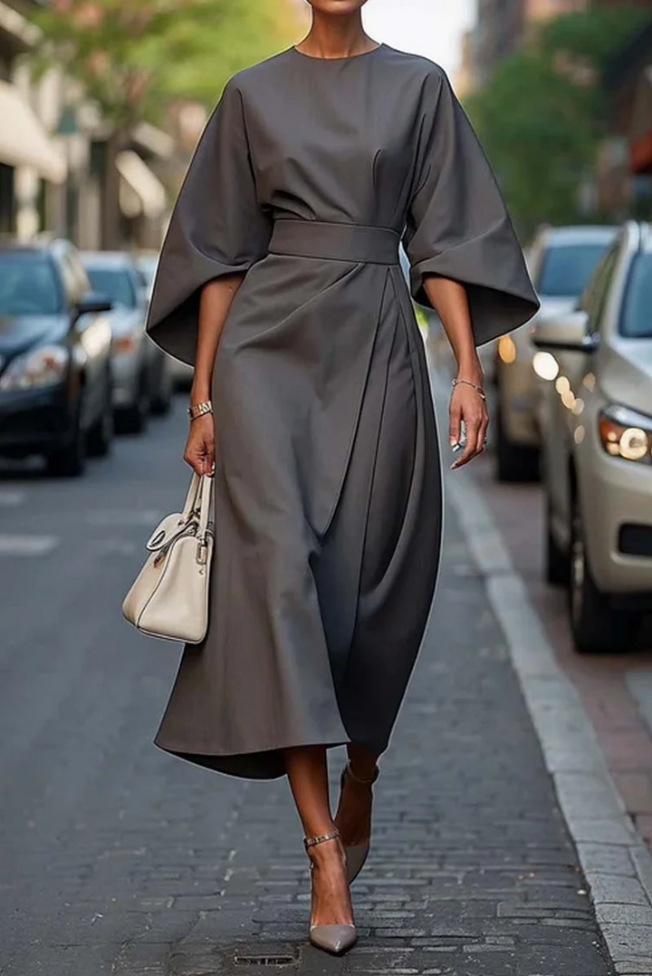 Three quarter view of a model in a grey elegant knee-length dress with wide lantern sleeves and a wrap skirt design