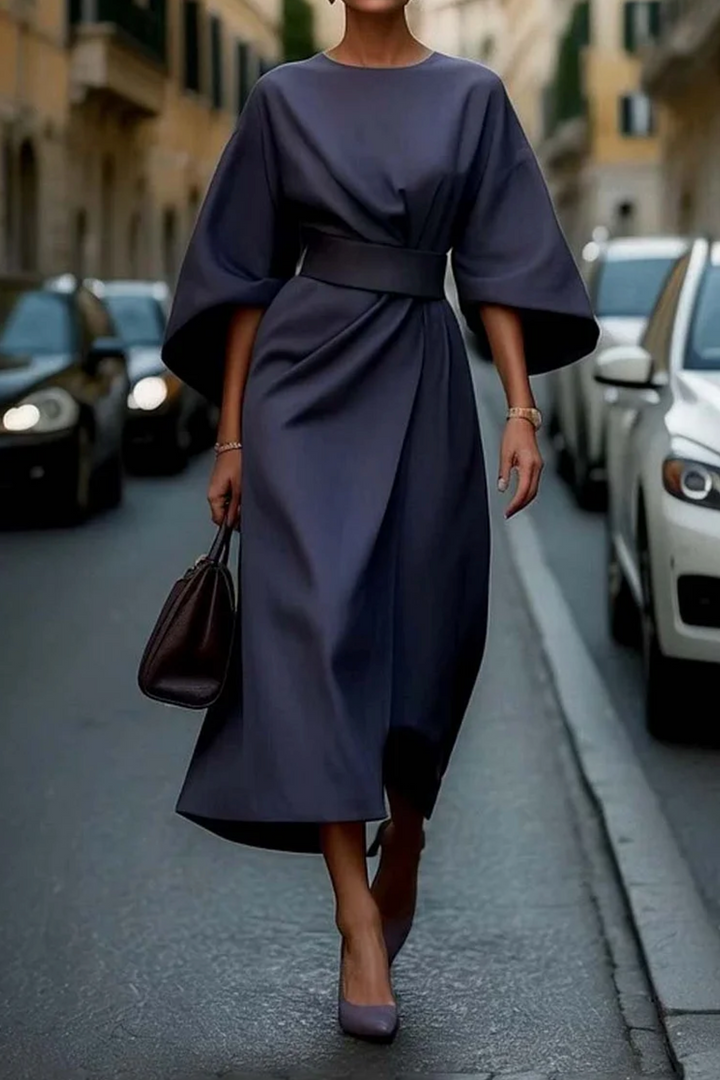 Front view of a model in a charcoal elegant knee-length dress with wide lantern sleeves and a wrap skirt design