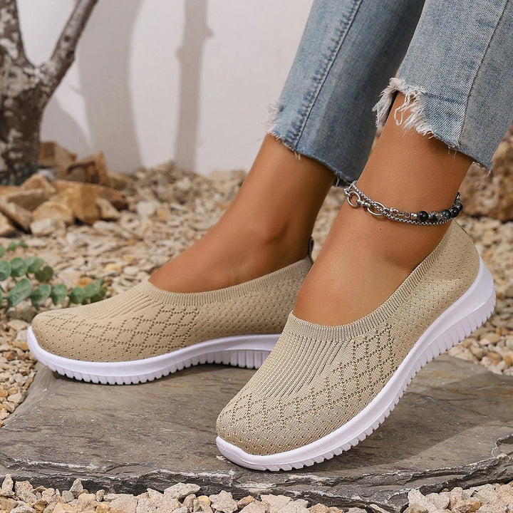 Close up of a model wearing beige breathable mesh flats with white soles and a silver ankle bracelet
