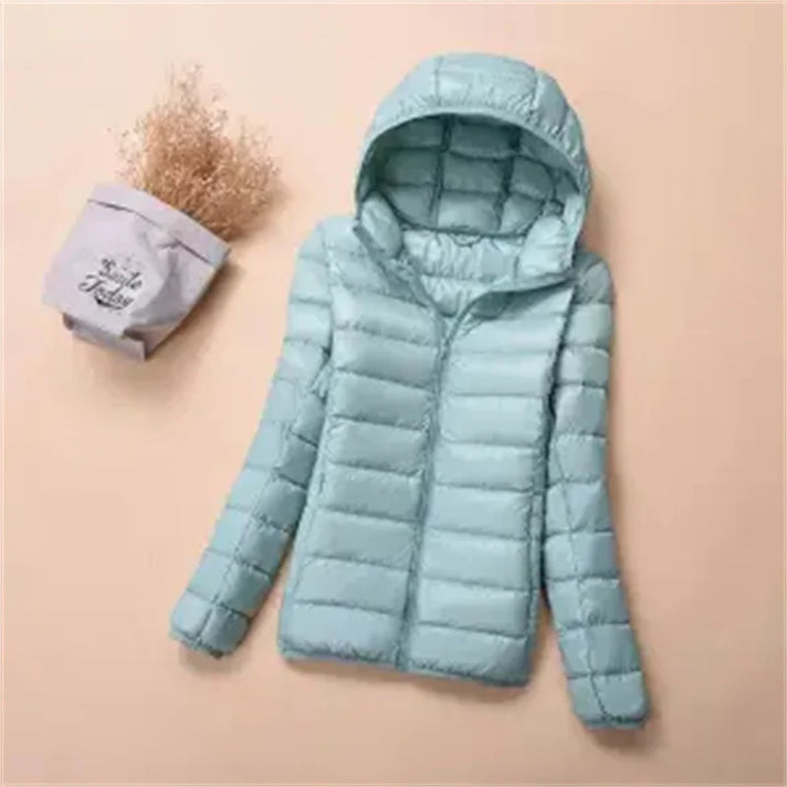 Front view of a mint hooded lightweight puffer jacket with a zipper, next to dried flowers in a bag