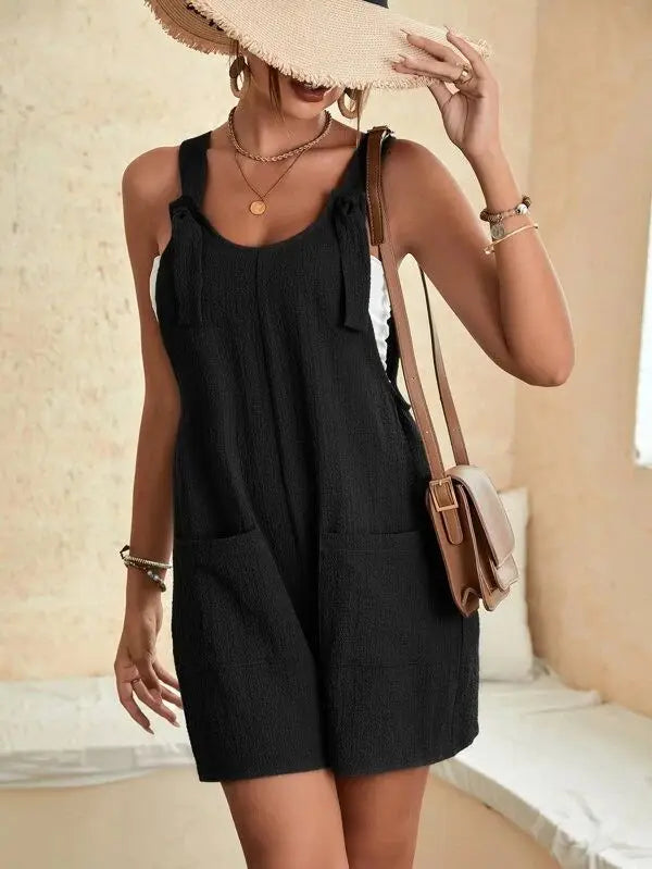 Three quarter view of a woman wearing a black casual sleeveless summer romper with tie straps and pockets