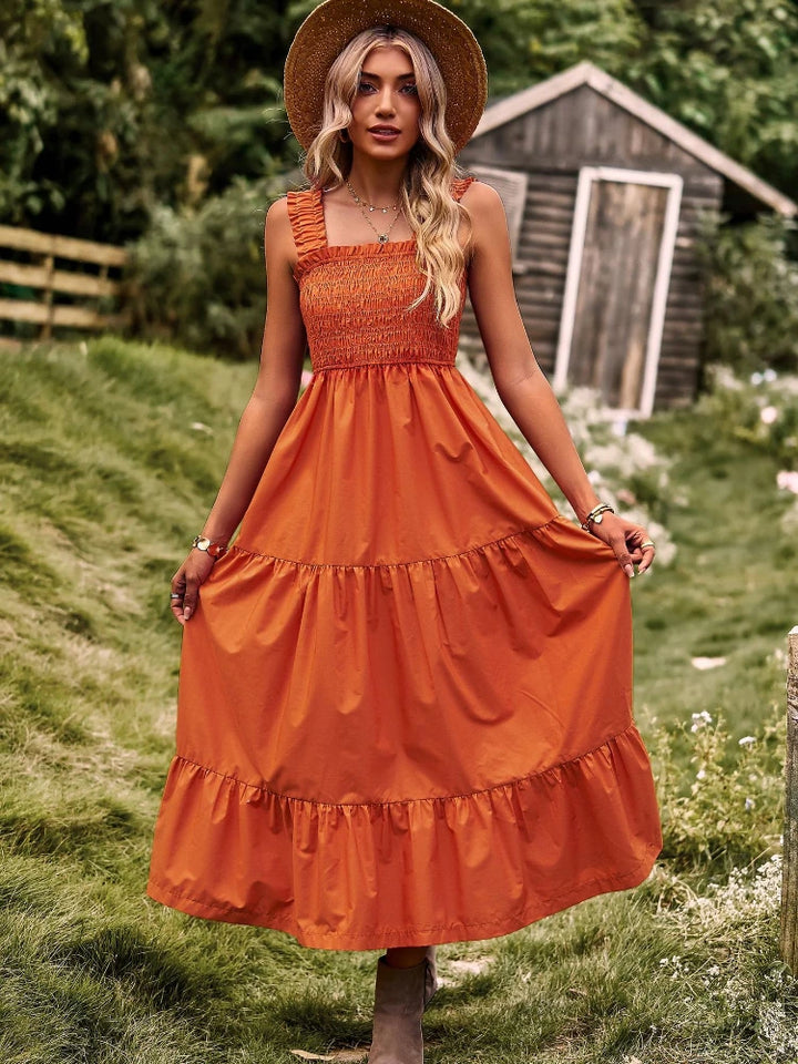 Front view of a model in an orange sleeveless halter maxi dress with a square neckline and tiered skirt