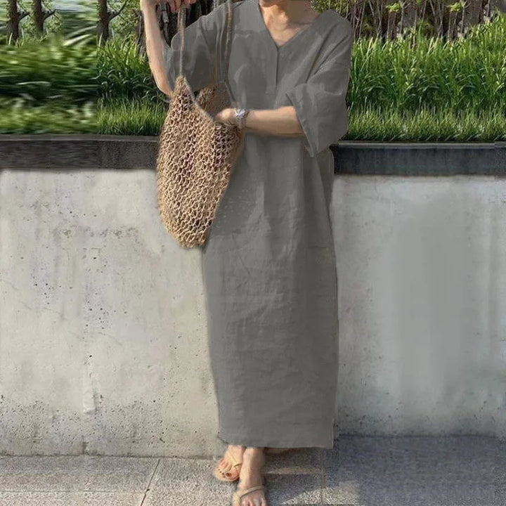 Front view, model wearing the cotton linen V-neck maxi dress in charcoal with a woven net bag and sandals