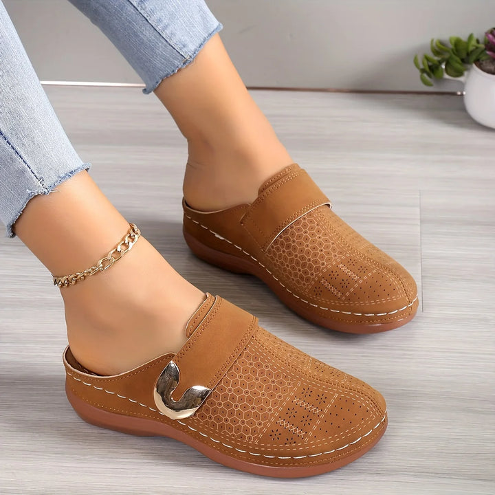 Close up, a woman wears tan orthopaedic wedge sandals with gold detail and perforated pattern