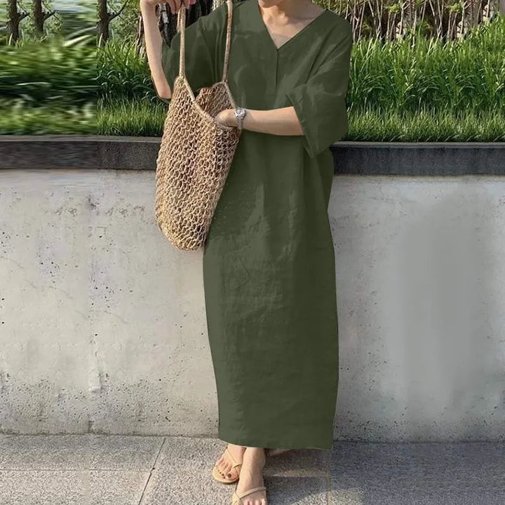 Front view, model wearing the cotton linen V-neck maxi dress in olive with a woven net bag and sandals