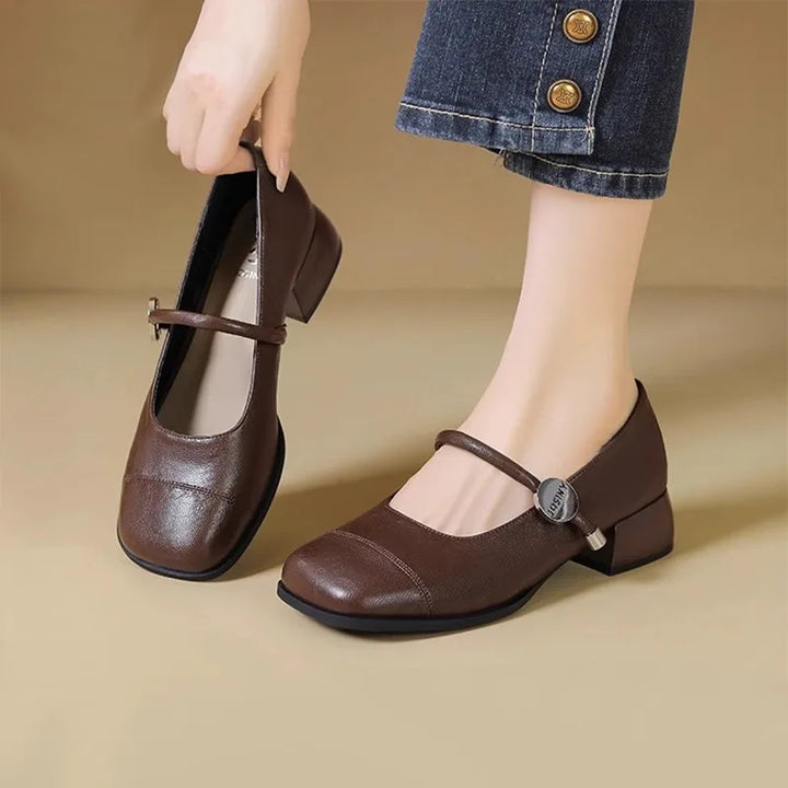 Worn by model, a woman holds one brown square toe Mary Jane shoe while wearing another on her foot