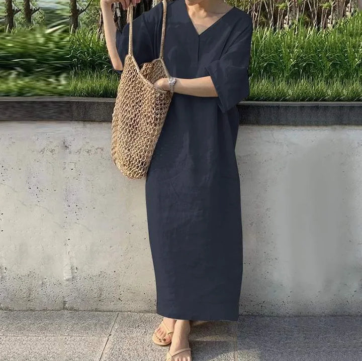 Front view, model wearing the cotton linen V-neck maxi dress in navy with a woven net bag and sandals