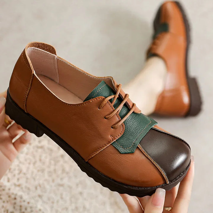 Close up of a Nora genuine leather flat held by hands, showing brown, dark brown, and green panels