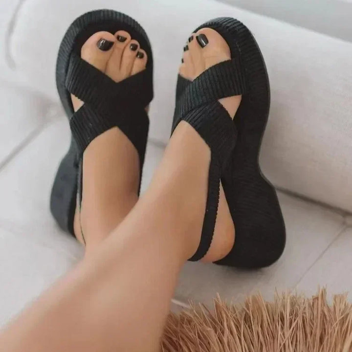 Back view of black modern chunky Roman sandals with velvet upper, worn by model, showing black toenails