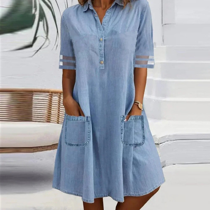 Front view of a model wearing a light blue denim midi dress with a collar, button placket, and two large pockets