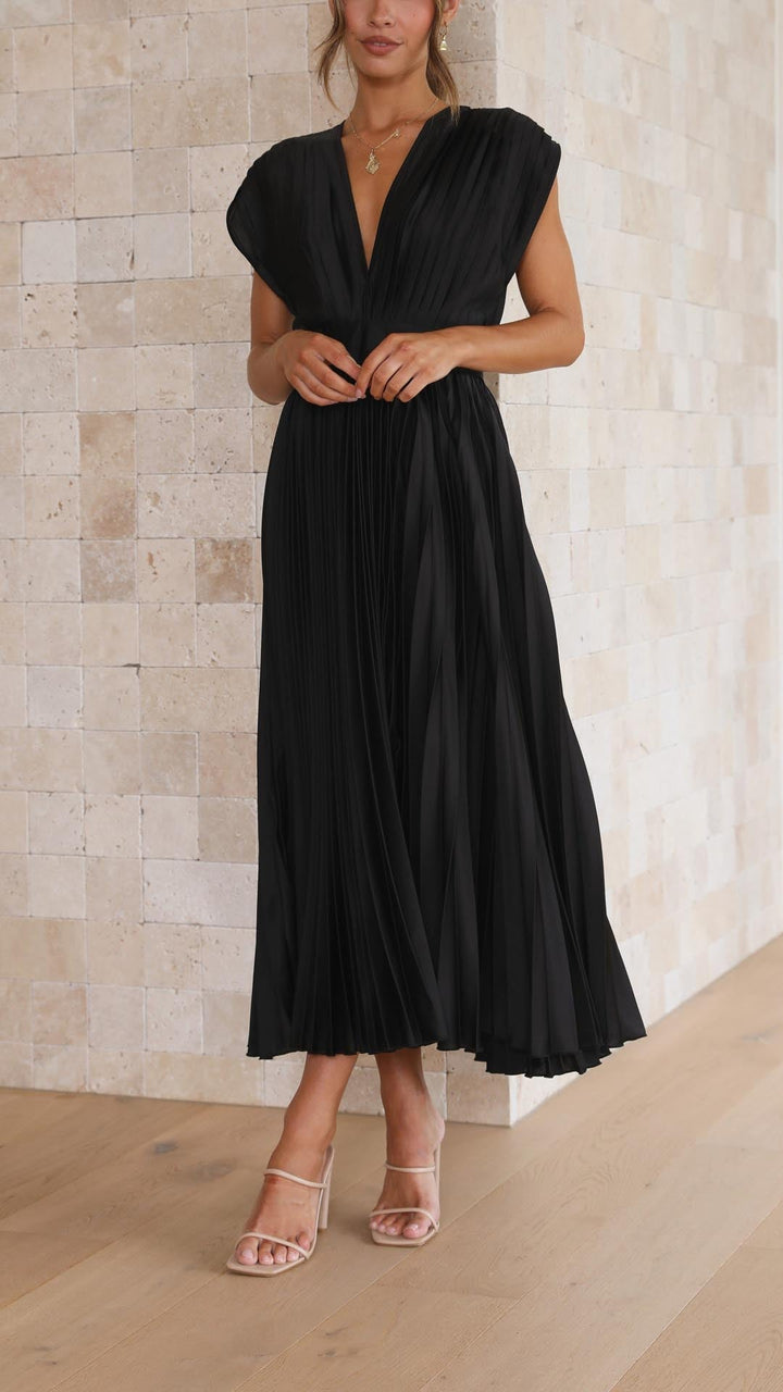 Front view of a model wearing an elegant pleated dress, hands clasped, highlighting the V-neck and high waist