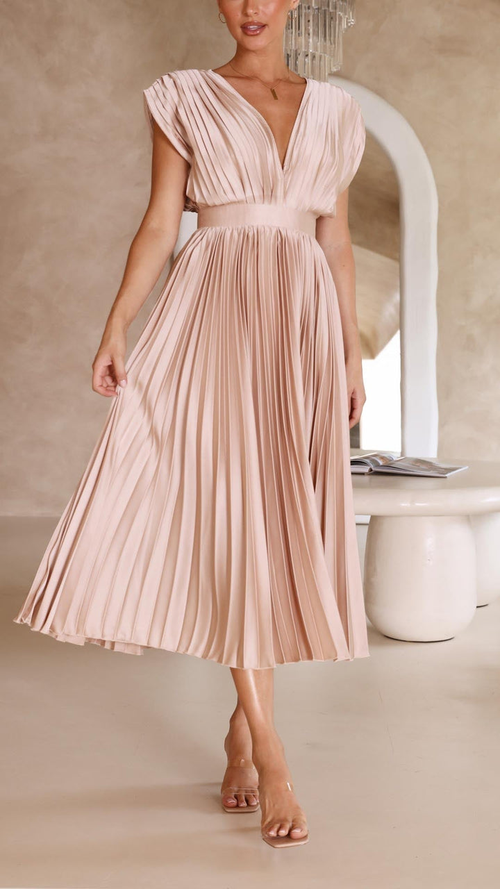 Front view of a model wearing an elegant pleated dress, gently touching the pleated skirt with one hand