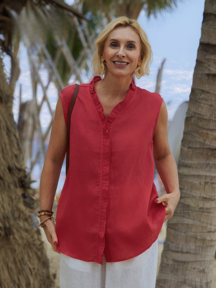 Front view, model wearing a red linen sleeveless ruffle shirt with white linen pants, by palm trees