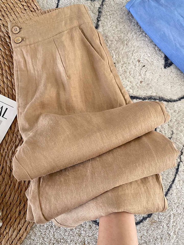Close up of beige cotton linen casual pants with button details and folded legs, held by a hand