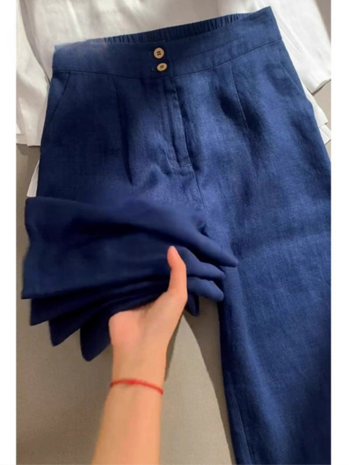 Close up of blue cotton linen casual pants with two buttons and a hand holding the folded leg