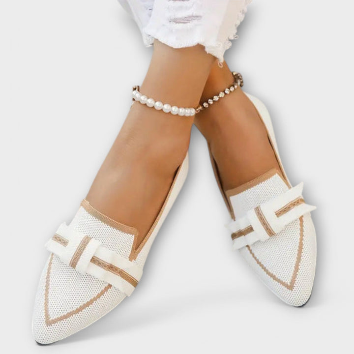 Close up of a model wearing white knotted flat loafer shoes with gold trim and pearl anklets