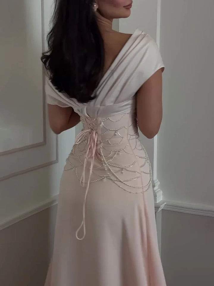 Back view of a model in a pearl beaded off-shoulder evening gown with a laced-up corset detail