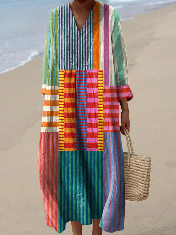Front view of a model wearing a colourful geometric pattern art print cotton dress with a woven bag on a sandy beach