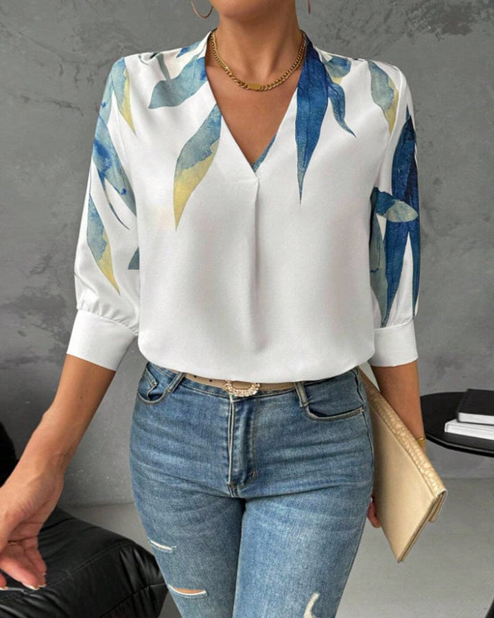 Front view of a woman wearing a white V-neck blouse with a blue and yellow leaf print and jeans