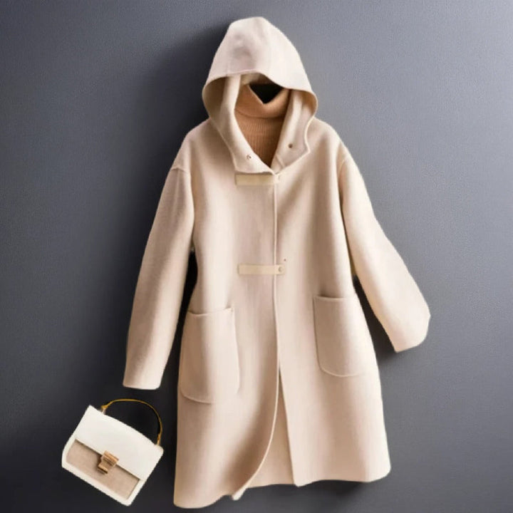 Front view of a cream soft wool coat with a hood and toggle details, styled with a beige turtleneck and handbag