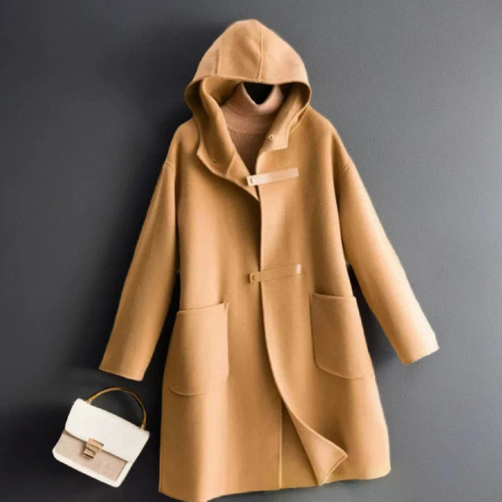 Front view of a camel soft wool coat with a hood and toggle closures, styled with a beige turtleneck and handbag