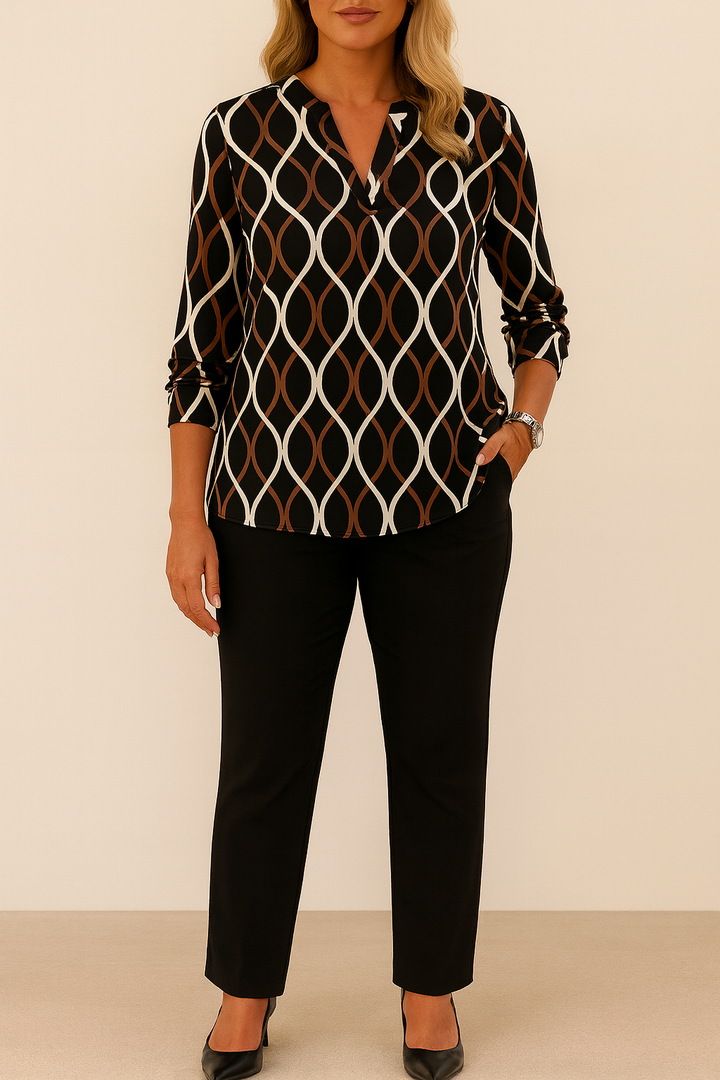 Worn by model, a geometric print V-neck blouse with long sleeves and black pants, one hand in pocket