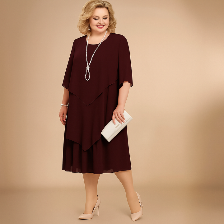 Three quarter front view of a woman wearing a layered maroon elegant dress with a pearl necklace and clutch bag