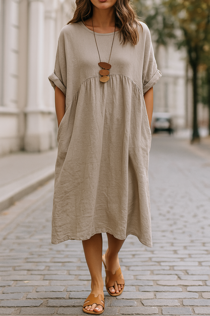 Front three quarter view of a model wearing a taupe round neck 3/4 sleeve boho dress with pockets and sandals