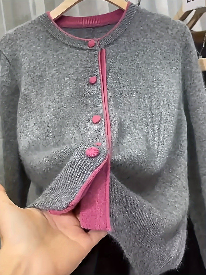 Close up of a grey knitted cardigan with pink trim and buttons, held at the hem