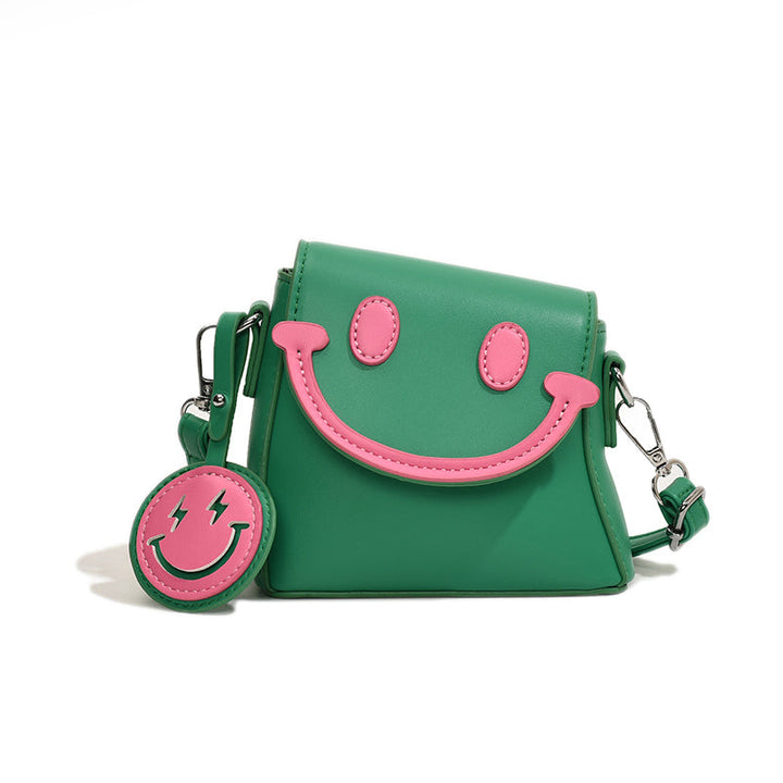 Front view of a green Bright Smile crossbody bag with pink smiley face and keyring against a white background