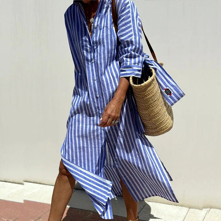 Three quarter view, model wearing a blue and white striped shirt dress with a straw bag over her shoulder