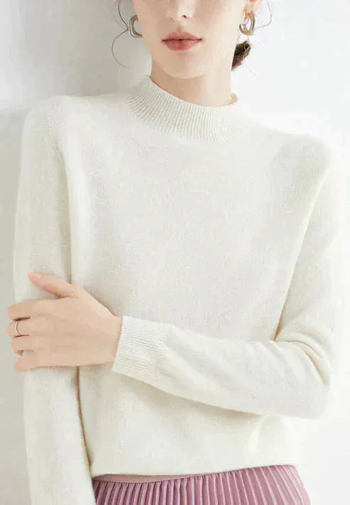 Close up, model wearing a white cashmere mock-neck jumper with ribbed collar and cuffs, pink pleated skirt