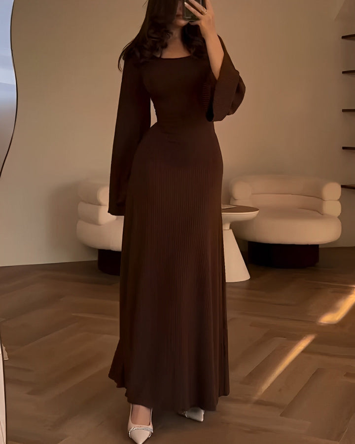 Front view of a model in a dark elegant knit maxi dress with a square neckline and flare sleeves, holding a phone