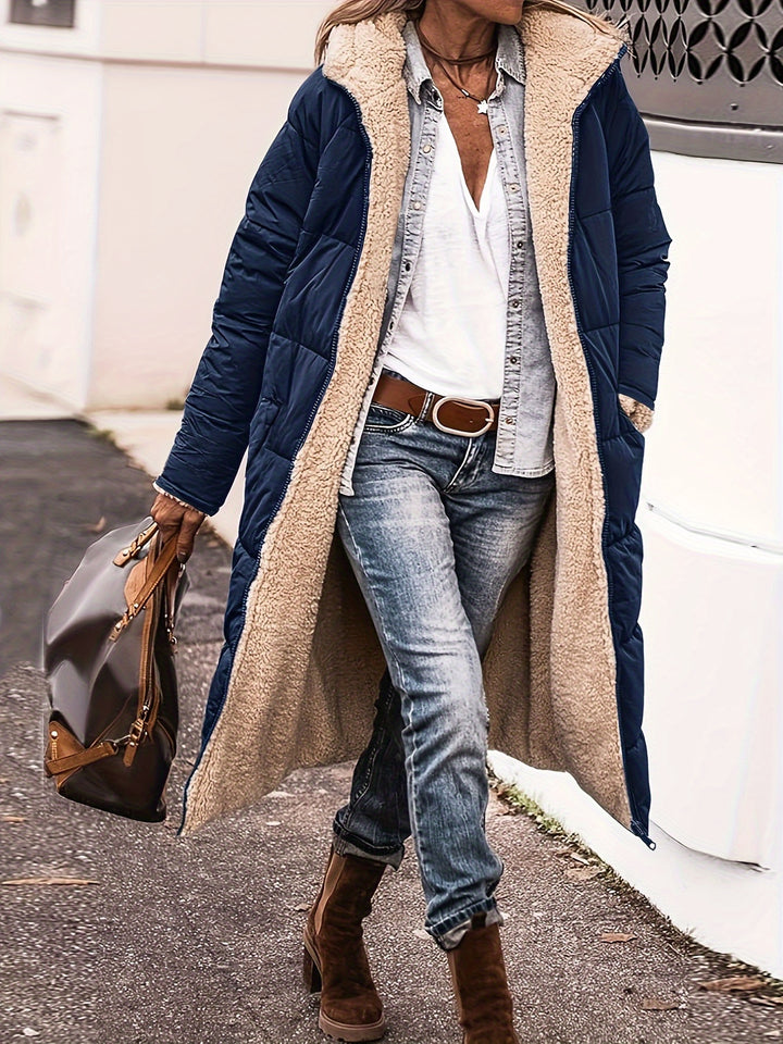 Three quarter view, model wearing a navy reversible quilted hooded coat with cream sherpa lining, jeans, and boots
